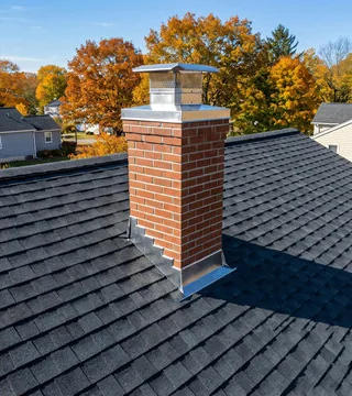 After: new red brick chimney with a stainless cap on a clean roof among autumn trees